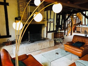 Ein traditionelles Interieur mit freiliegenden Balken, einem Kamin, Ledermöbeln und einer Treppe.