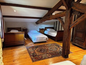 Ein Schlafzimmer mit zwei Betten, Holzbalken, einem gemusterten Teppich und einer Deckenleuchte.