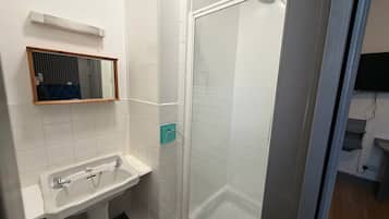Un baño con lavamanos blanco, espejo y cabina de ducha.