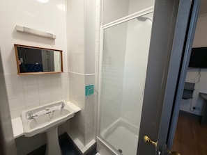 Et badeværelse med en hvid vask, et spejl og en bruseniche.
