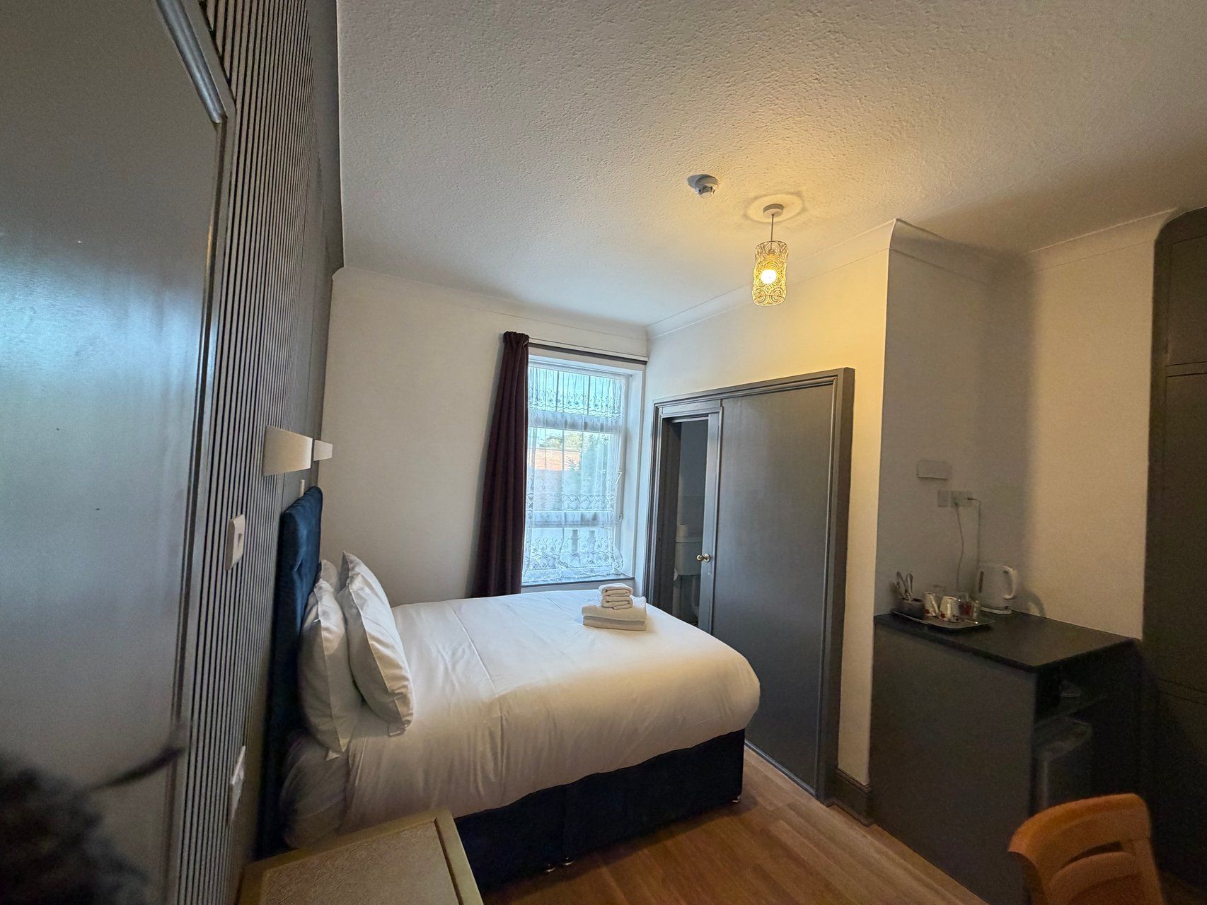 A hotel room with a bed, a desk, a chair, a wardrobe, and a window.