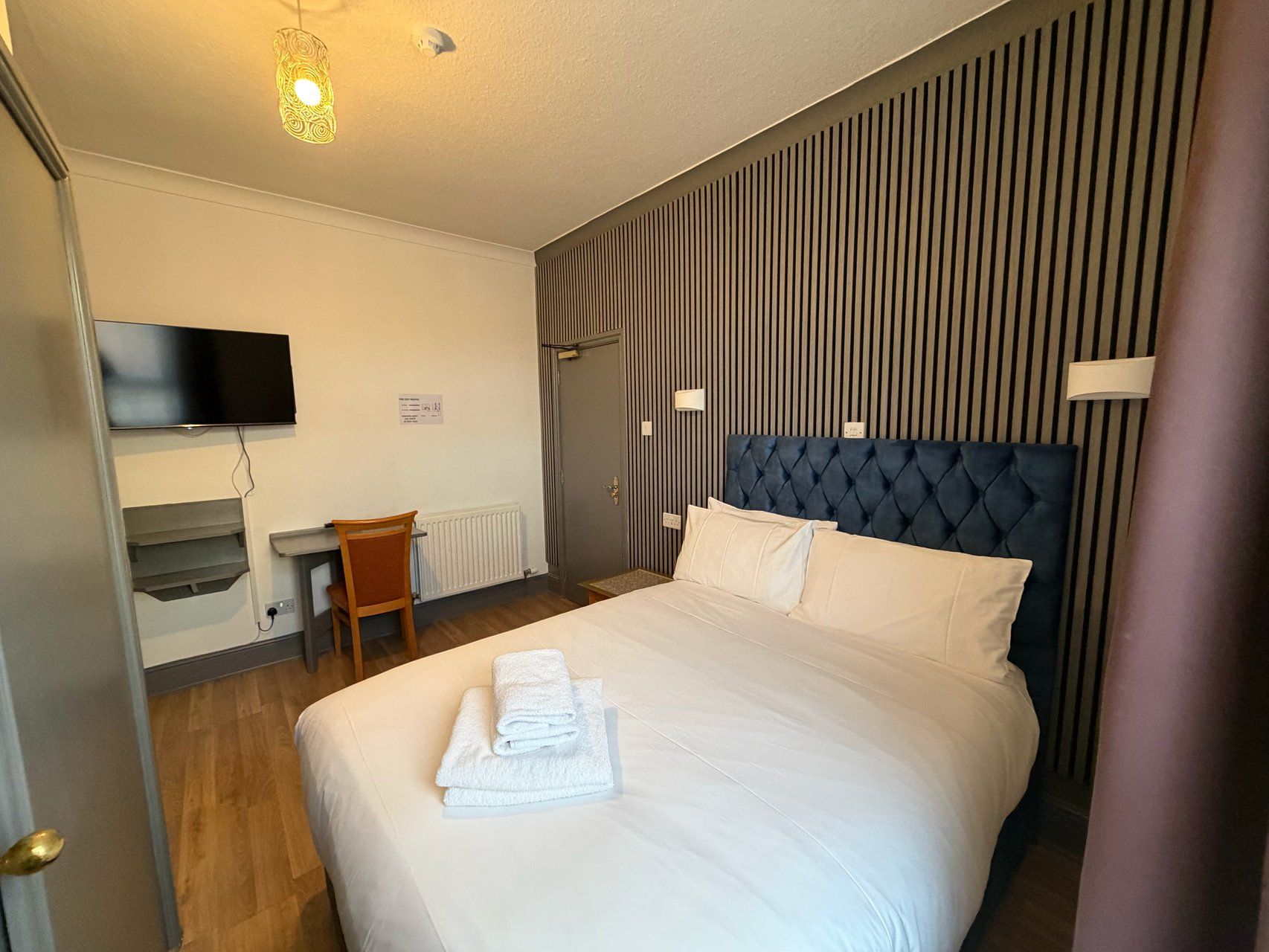 A hotel room with a bed, a desk, a chair, a television, and a door.
