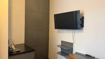 Et kompakt værelse med et fladskærms TV på væggen, en lille træstol og et tekøkken med en bordplade.