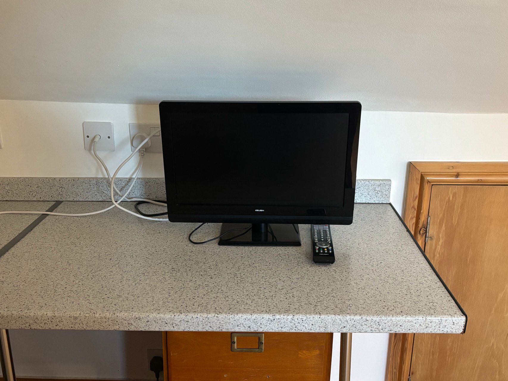 A flat-screen TV on a granite countertop with a remote control beside it.