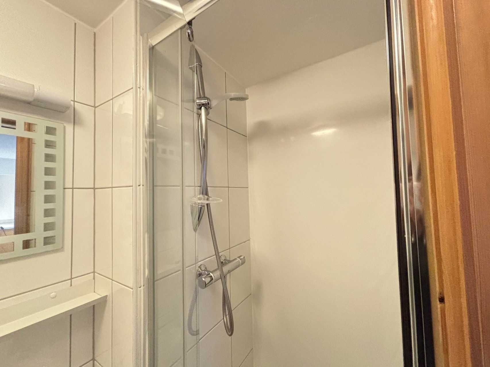 A shower with a glass door, a chrome showerhead, and a handheld shower attachment.