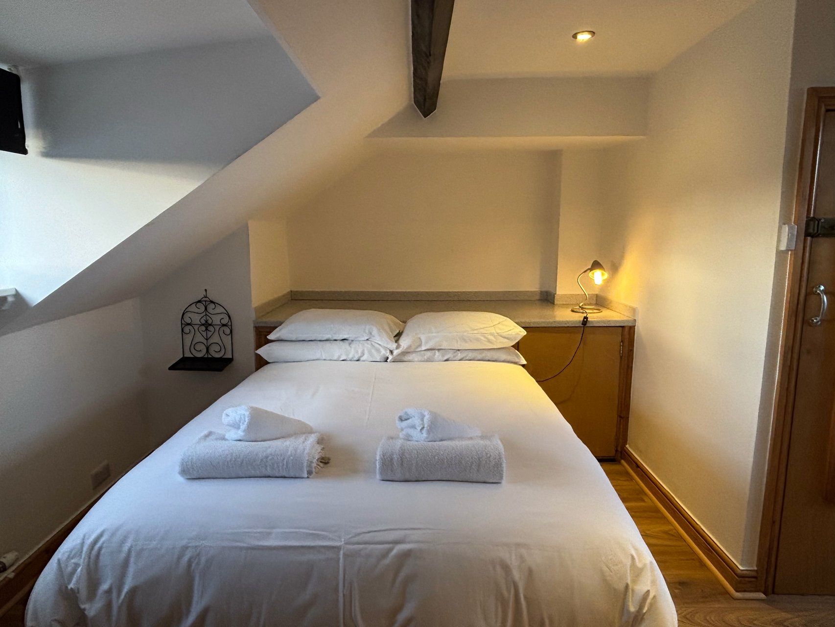 A hotel room with a bed, a nightstand, a lamp, and a decorative wall piece.