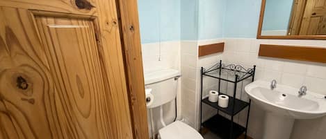Un baño con puerta de madera, inodoro, lavabo y repisa con papel higiénico.