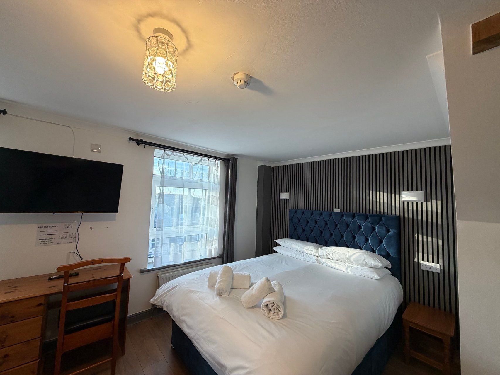 A hotel room with a bed, a desk, a television, and a window with curtains.