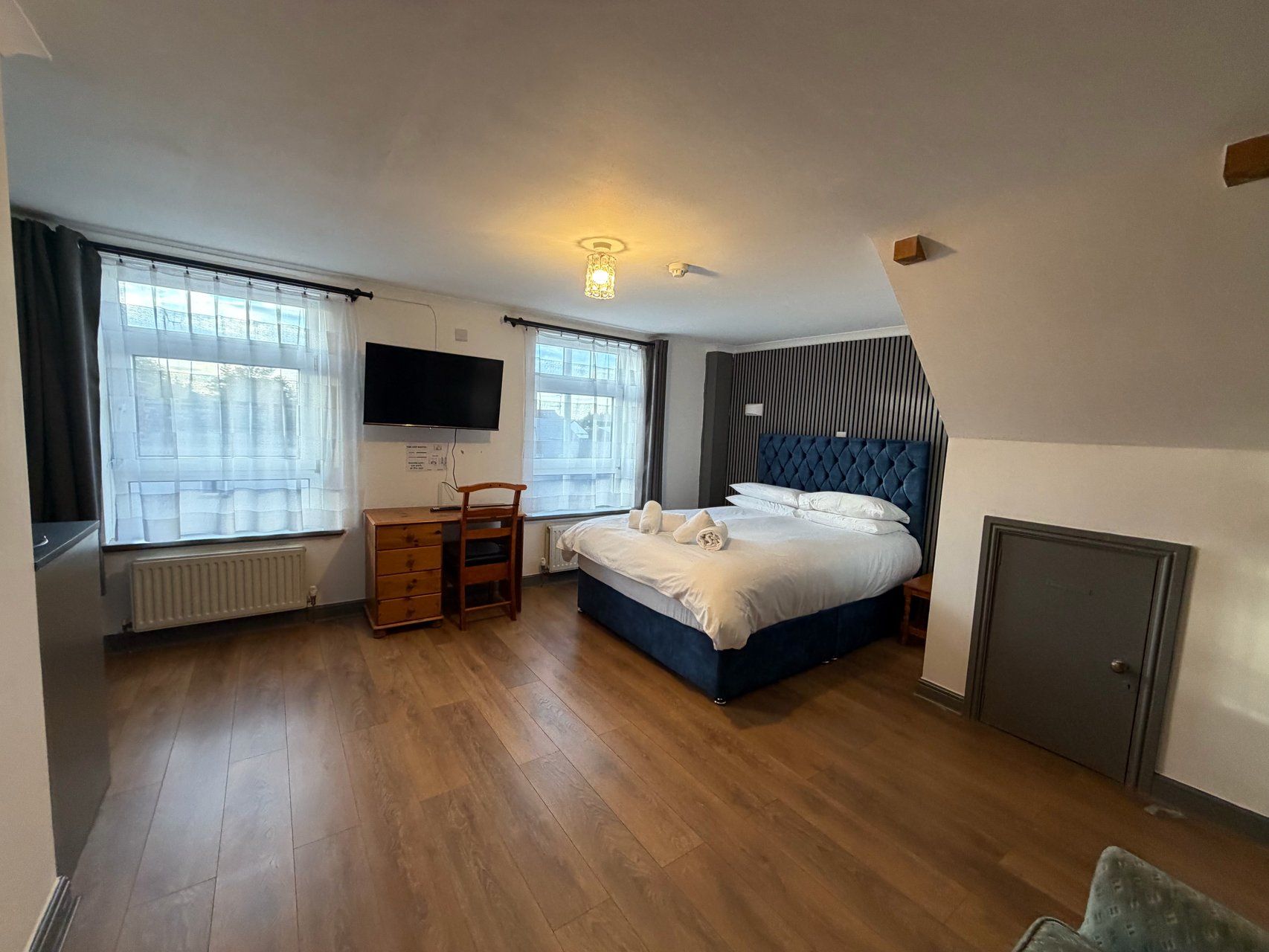 A bedroom with a bed, a desk, a chair, a television, and a radiator.