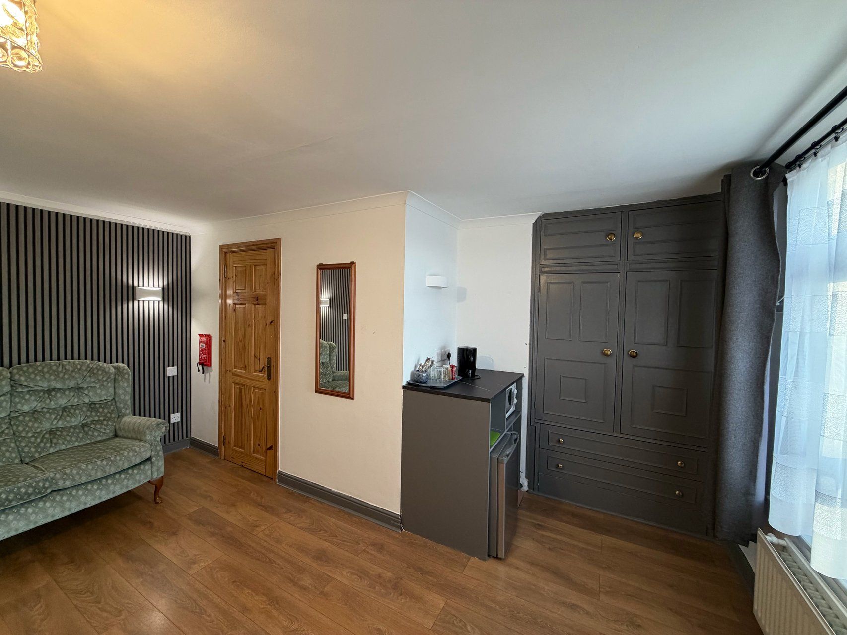 A room with a sofa, a wooden door, a mirror, a small kitchenette, and a wardrobe.