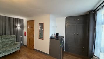 A room with a sofa, a wooden door, a mirror, a small kitchenette, and a wardrobe.