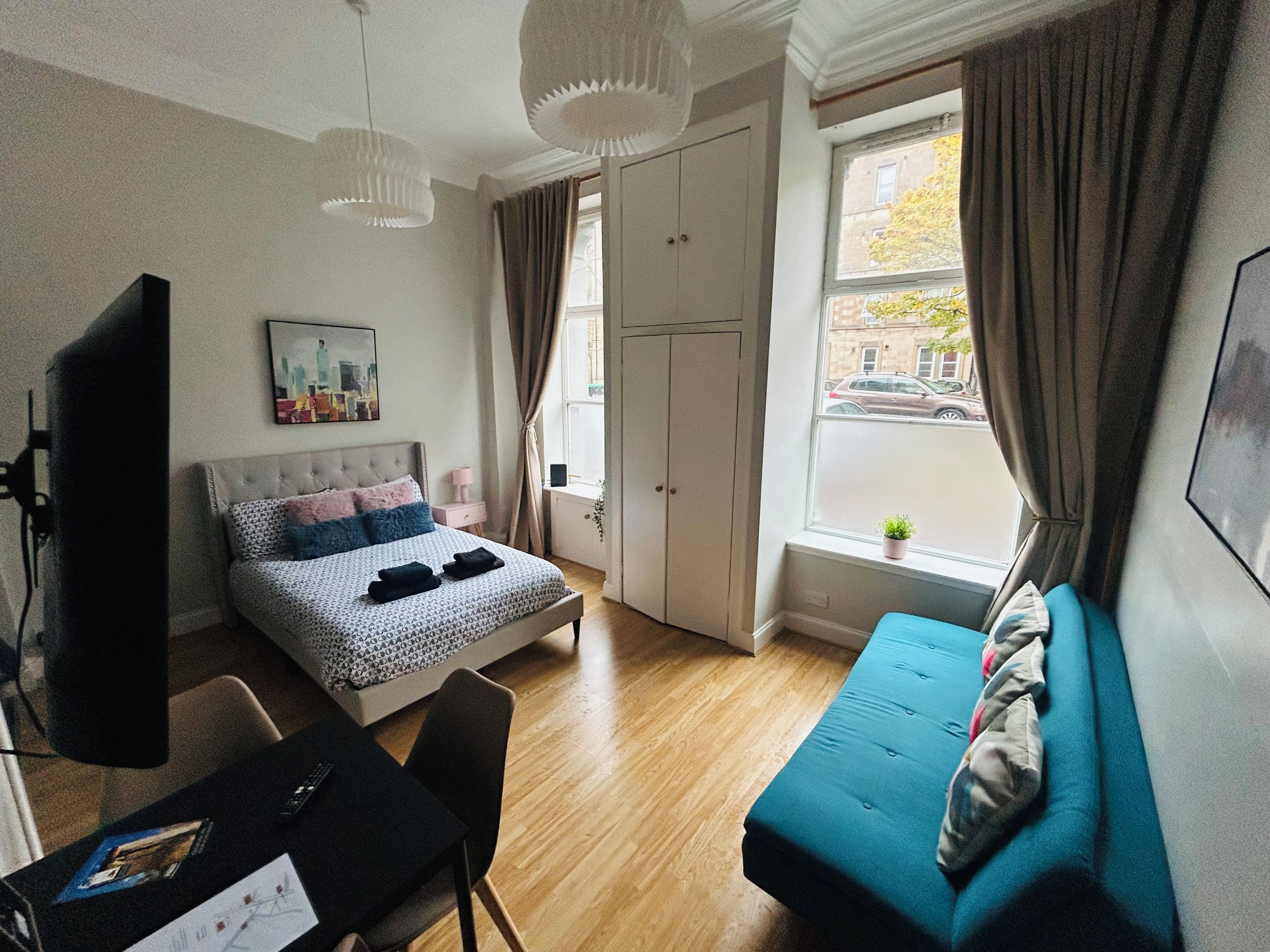 Ein Schlafzimmer mit Bett, Schreibtisch, Stuhl, Sofa, einem Fenster mit Vorhängen und einer Tür.