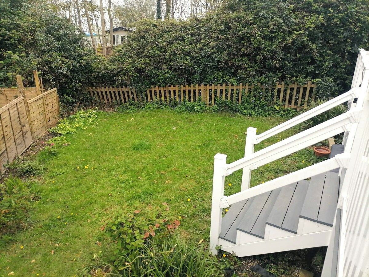 Ein Garten mit Holzzaun, Rasenfläche und einer weißen Treppe, die zu einer Terrasse führt.