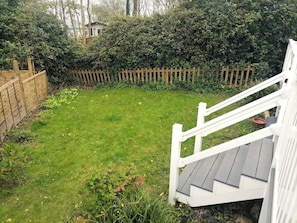 Ein Garten mit Holzzaun, Rasenfläche und einer weißen Treppe, die zu einer Terrasse führt.