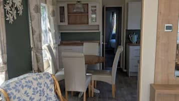 Un espacio habitable compacto con comedor, kitchenette y una silla de mimbre.