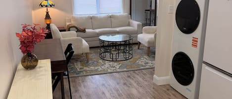 A compact living space with a sofa, coffee table, dining table, and a washing machine.