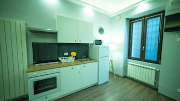 Une cuisine compacte avec des meubles blancs, un four à micro-ondes, un petit réfrigérateur et un plan de travail en bois.