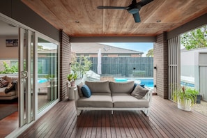 Ein überdachter Außenbereich mit Holzterrasse, einer Couch und einem Deckenventilator.