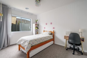 Ein Schlafzimmer mit einem Einzelbett, einem Schreibtisch, einem Stuhl, einem Bücherregal und einem Fenster mit Vorhängen.