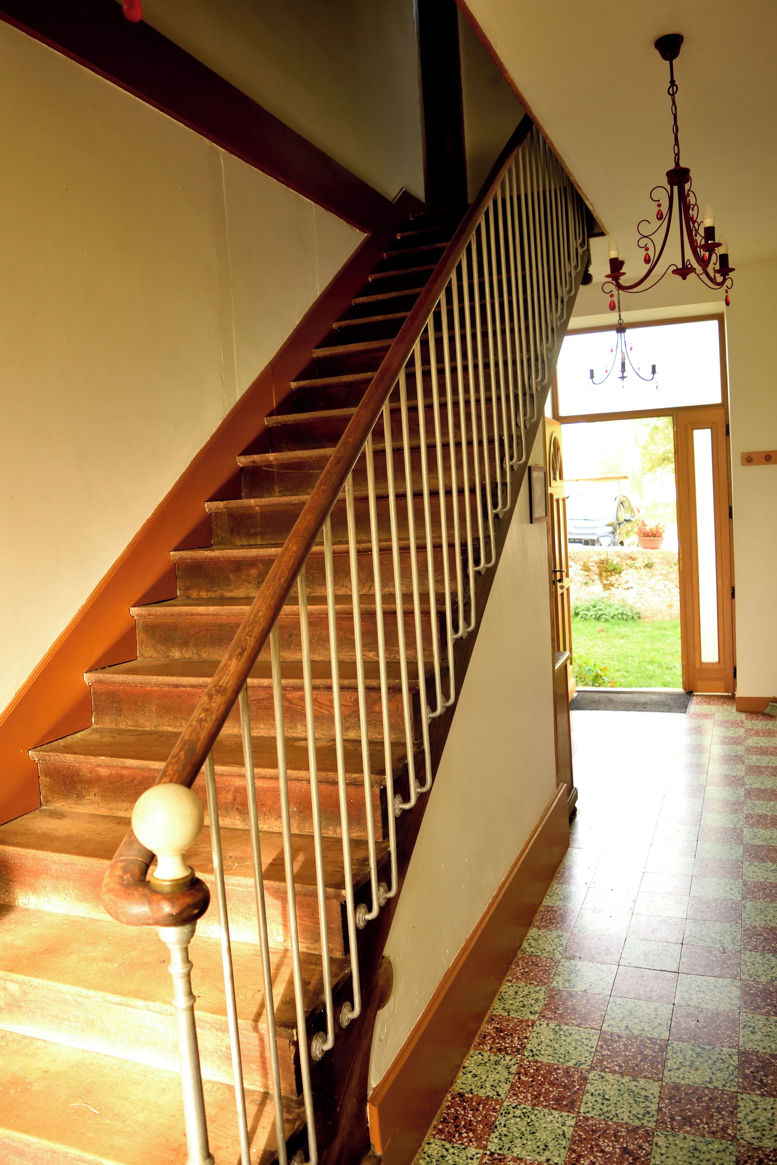 A wooden staircase with a metal handrail and a ball finial, leading to a door with a view of a garden.