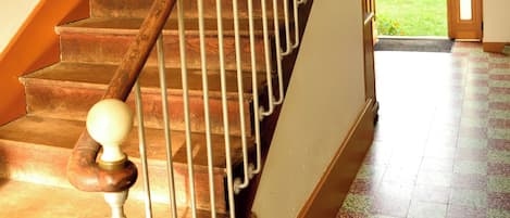 A wooden staircase with a metal handrail and a ball finial, leading to a door with a view of a garden.