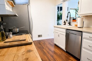 A modern kitchen with wooden flooring, stainless steel appliances, and white cabinetry.