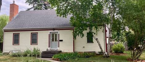 A single-story house with a front porch, a chimney, and a well-maintained garden.