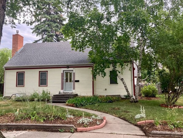 A single-story house with a front porch, a chimney, and a well-maintained garden.