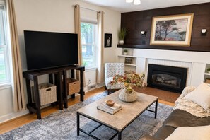 A living room with a flat-screen TV, a fireplace, a sofa, and a coffee table with a vase of flowers.