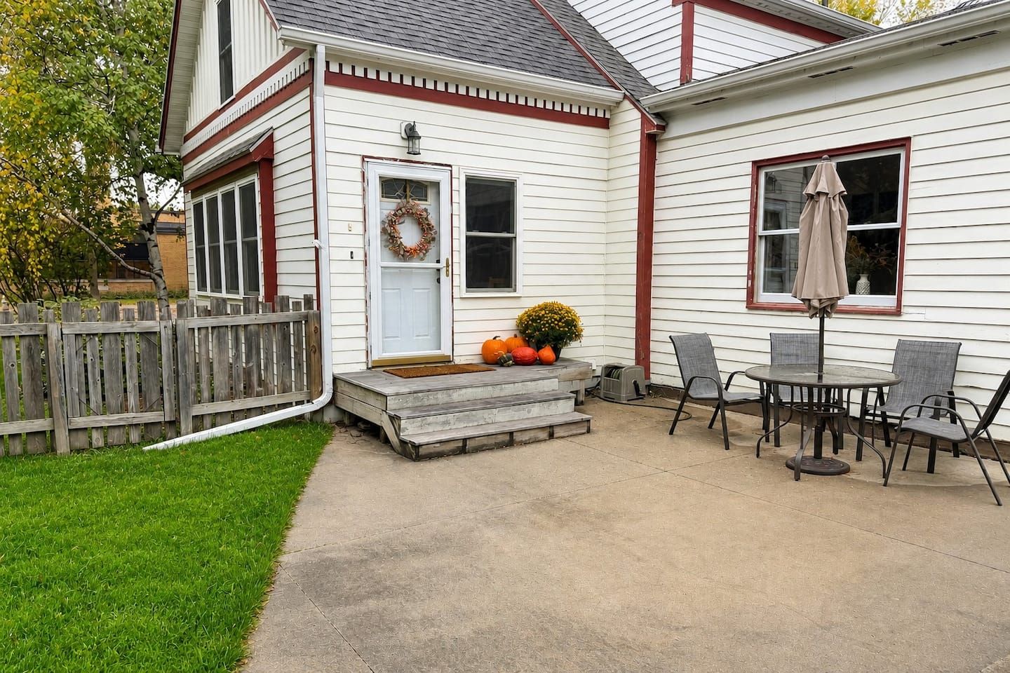 Une maison avec un porche à l’avant, une clôture en bois, une table avec des chaises et une guirlande décorative sur la porte.
