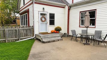 Une maison avec un porche à l’avant, une clôture en bois, une table avec des chaises et une guirlande décorative sur la porte.