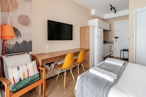 Een hotelkamer met een bed, een bureau, twee stoelen, een televisie, een koelkast en een kitchenette.