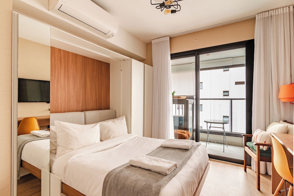 Habitació d'hotel amb llit, escriptori, cadira, televisió i un balcó amb taula i cadires.