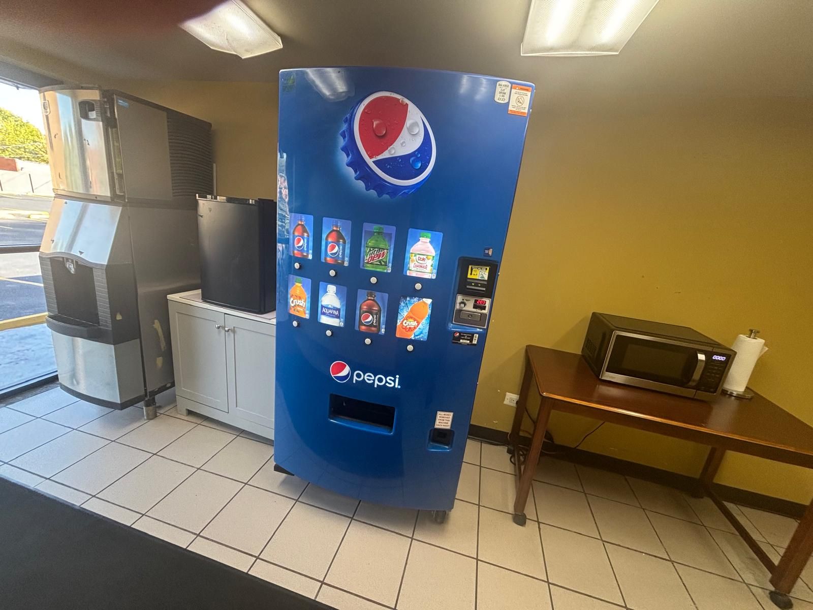 Una máquina expendedora con el logotipo de Pepsi, un microondas y un cubo de basura.