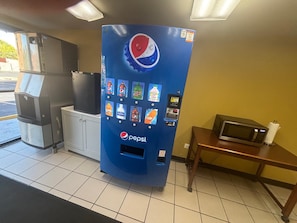 A vending machine with a Pepsi logo, a microwave, and a trash bin.