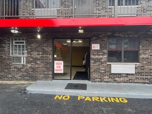 A building with a red awning, a 'NO PARKING' sign on the pavement, and a 'UNDER NEW MANAGEMENT' sign on the door.