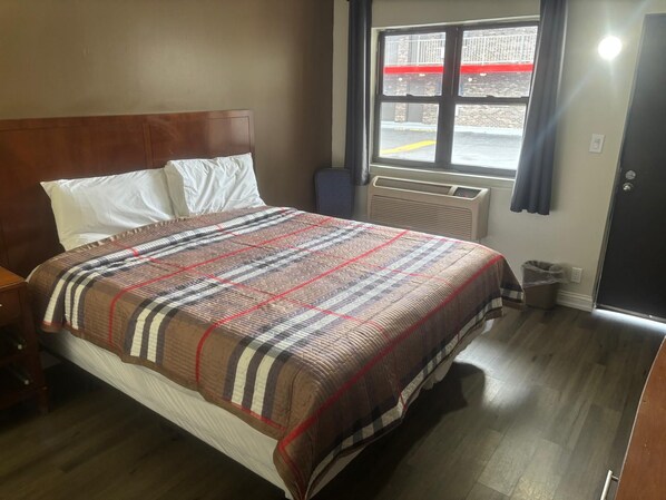 A hotel room with a bed, a window with a view of a parking lot, a heater, and a door.