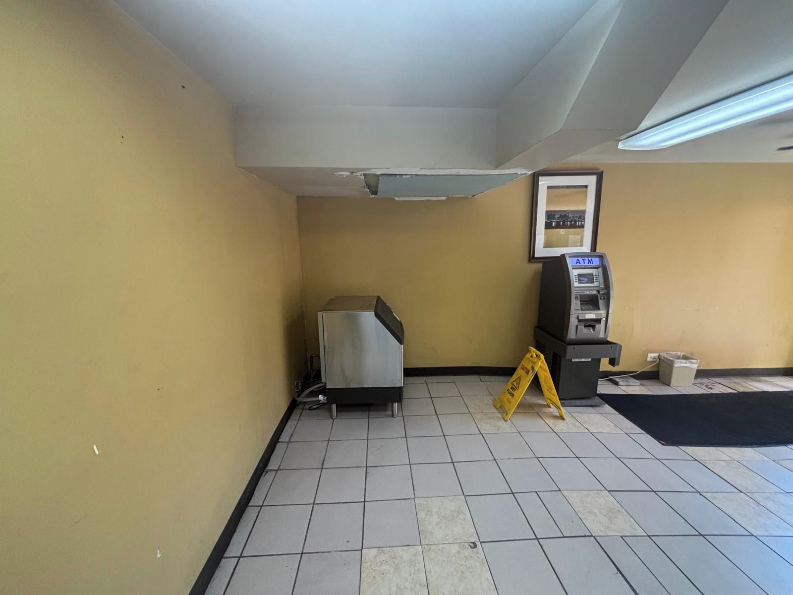 Una habitación con piso de baldosas, un objeto metálico, un cajero automático y un letrero de precaución.