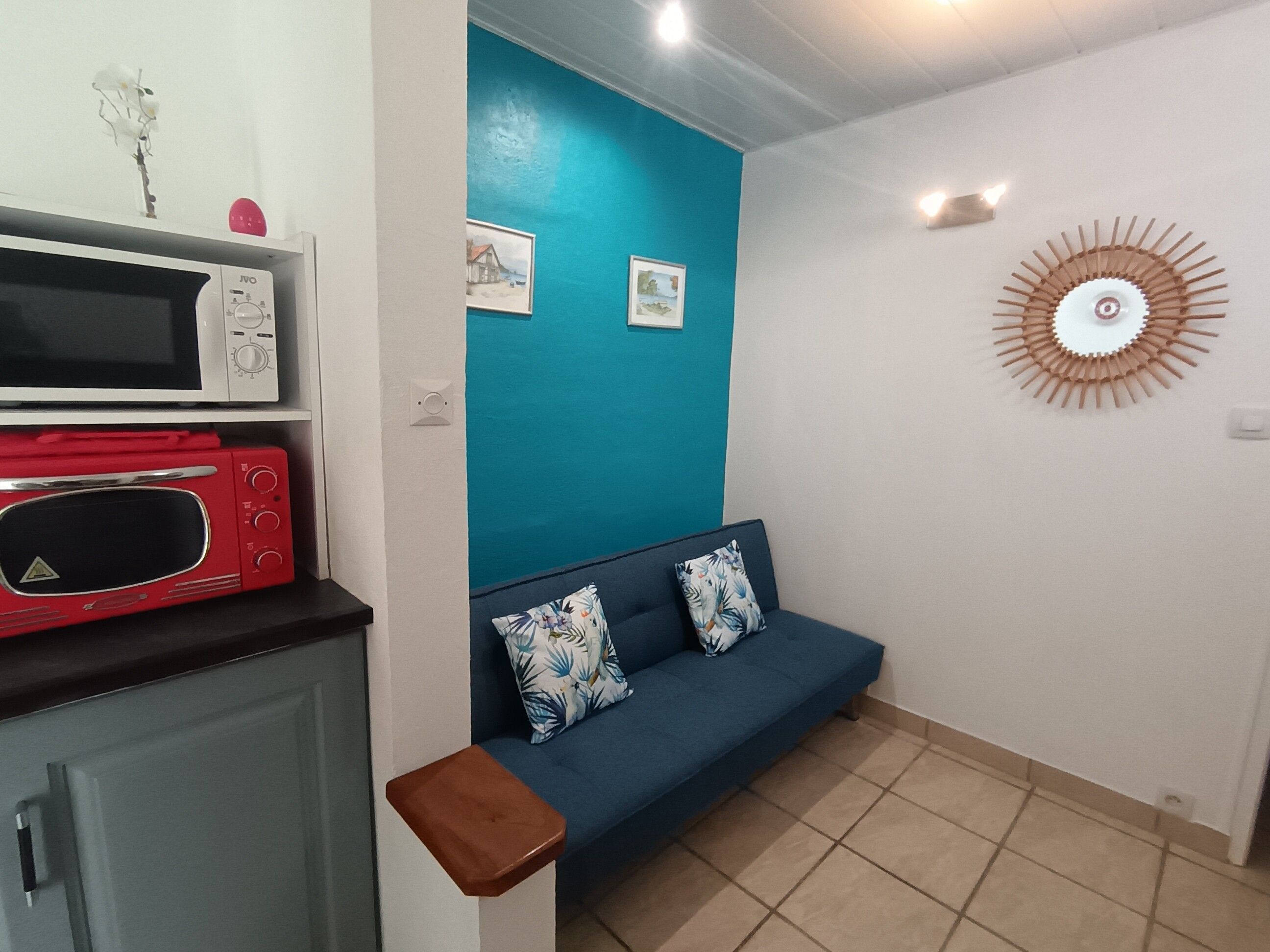 Una habitación con un sofá azul, un microondas rojo, un microondas blanco y un reloj de pared.