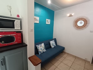 Une pièce avec un canapé bleu, un four à micro-ondes rouge, un four à micro-ondes blanc et une horloge murale.