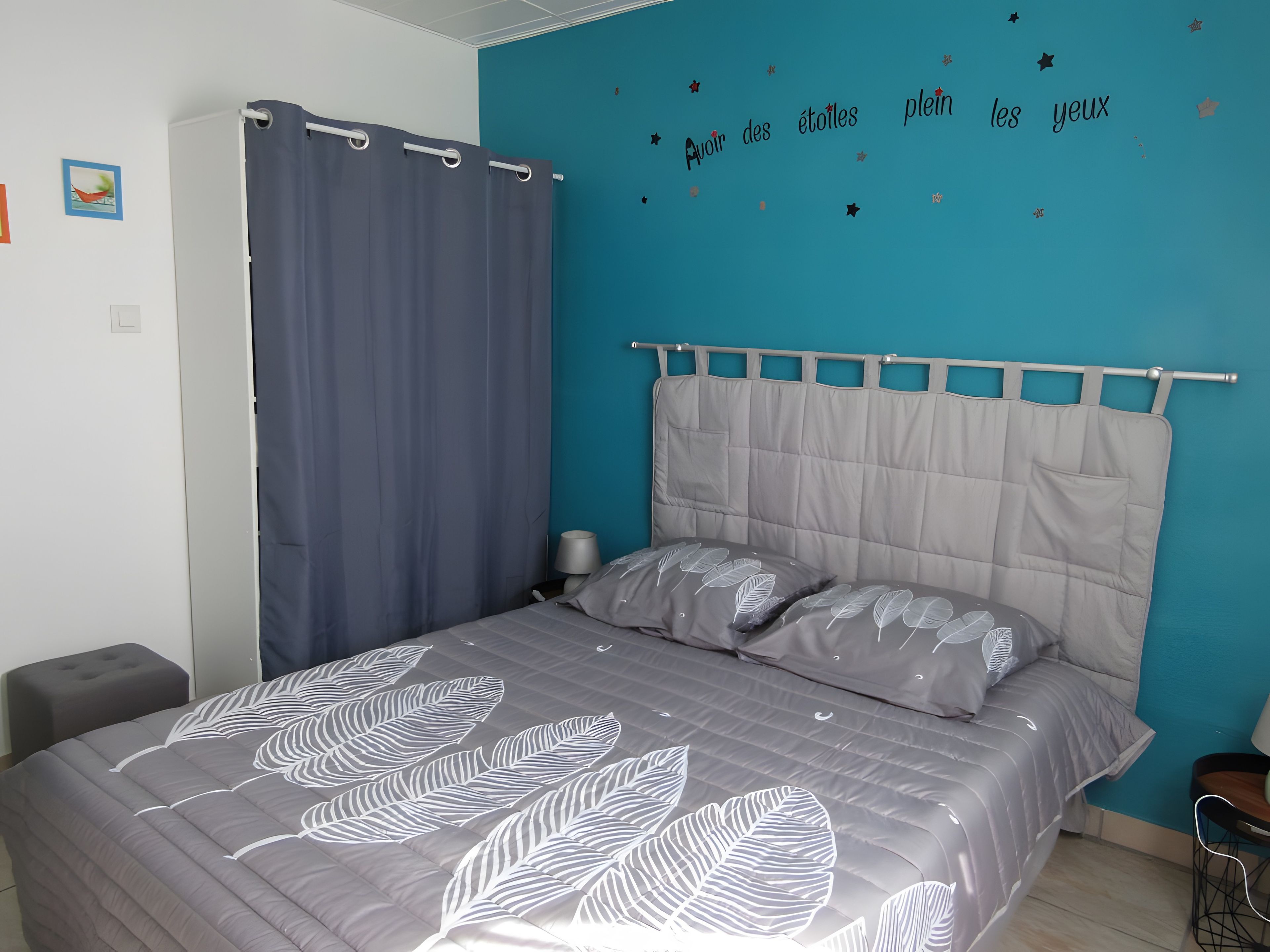 A bedroom with a bed, a nightstand, a chair, a curtain, and a wall with star decorations.