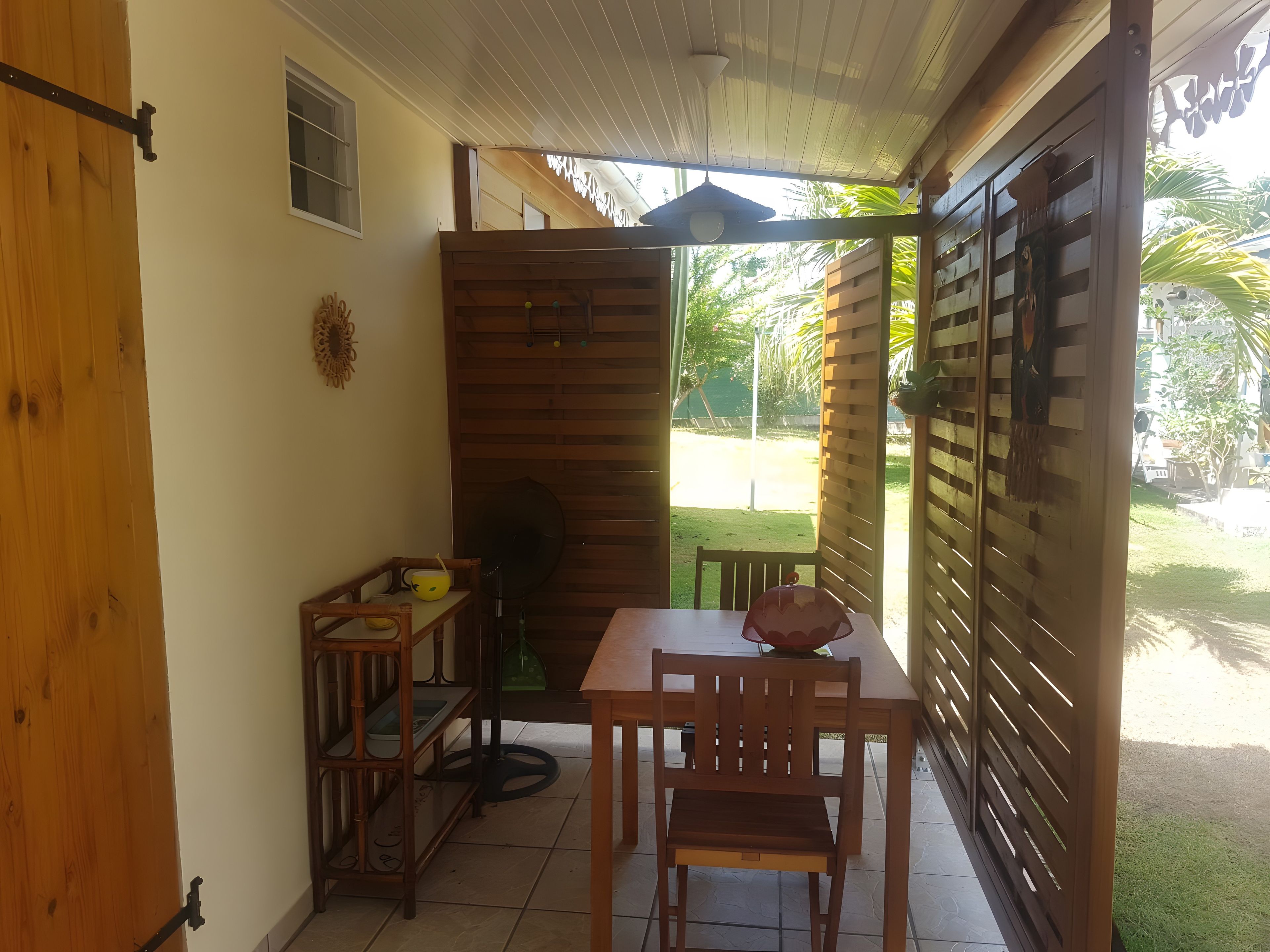 Un patio couvert comprenant une table et des chaises, un ventilateur et un meuble en bois.