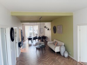 A spacious living area with a herringbone floor, a dining table with chairs, a sofa, and a coffee table. - New Listing (København)