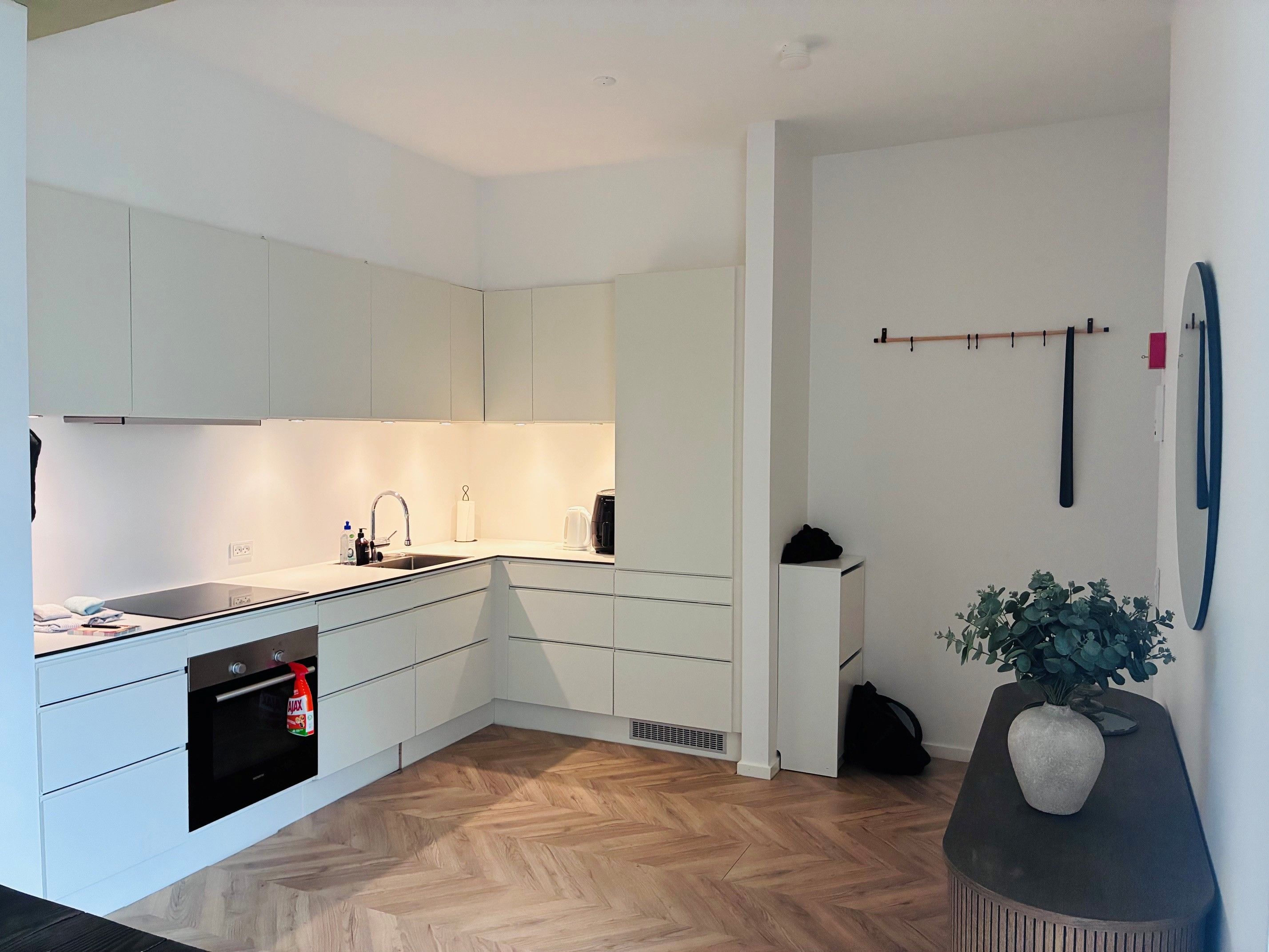 A modern kitchen with white cabinetry, a built-in oven, and a herringbone wood floor.