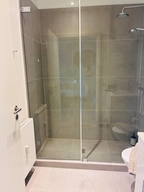 Et moderne badeværelse med et brusebadekar i glas, toilet og håndvask.