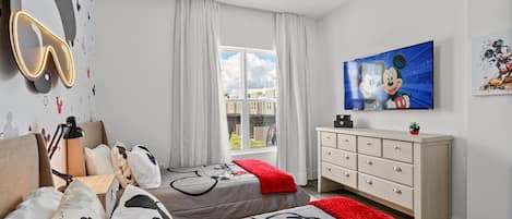 A bedroom with two beds, a dresser, a TV, and Mickey Mouse-themed decor.