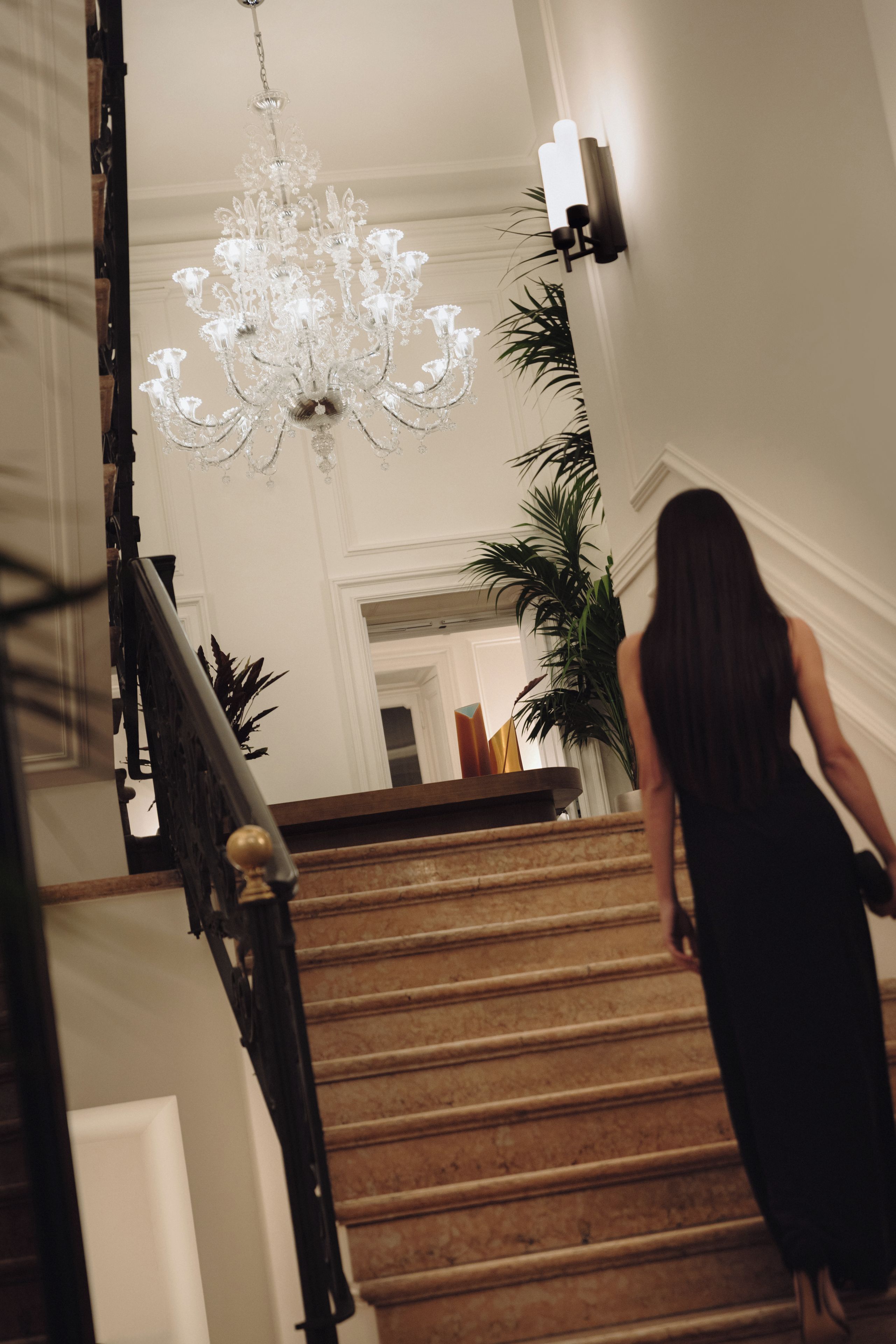 Un magnifique escalier orné d’un lustre, avec une plante en pot et une personne qui descend.