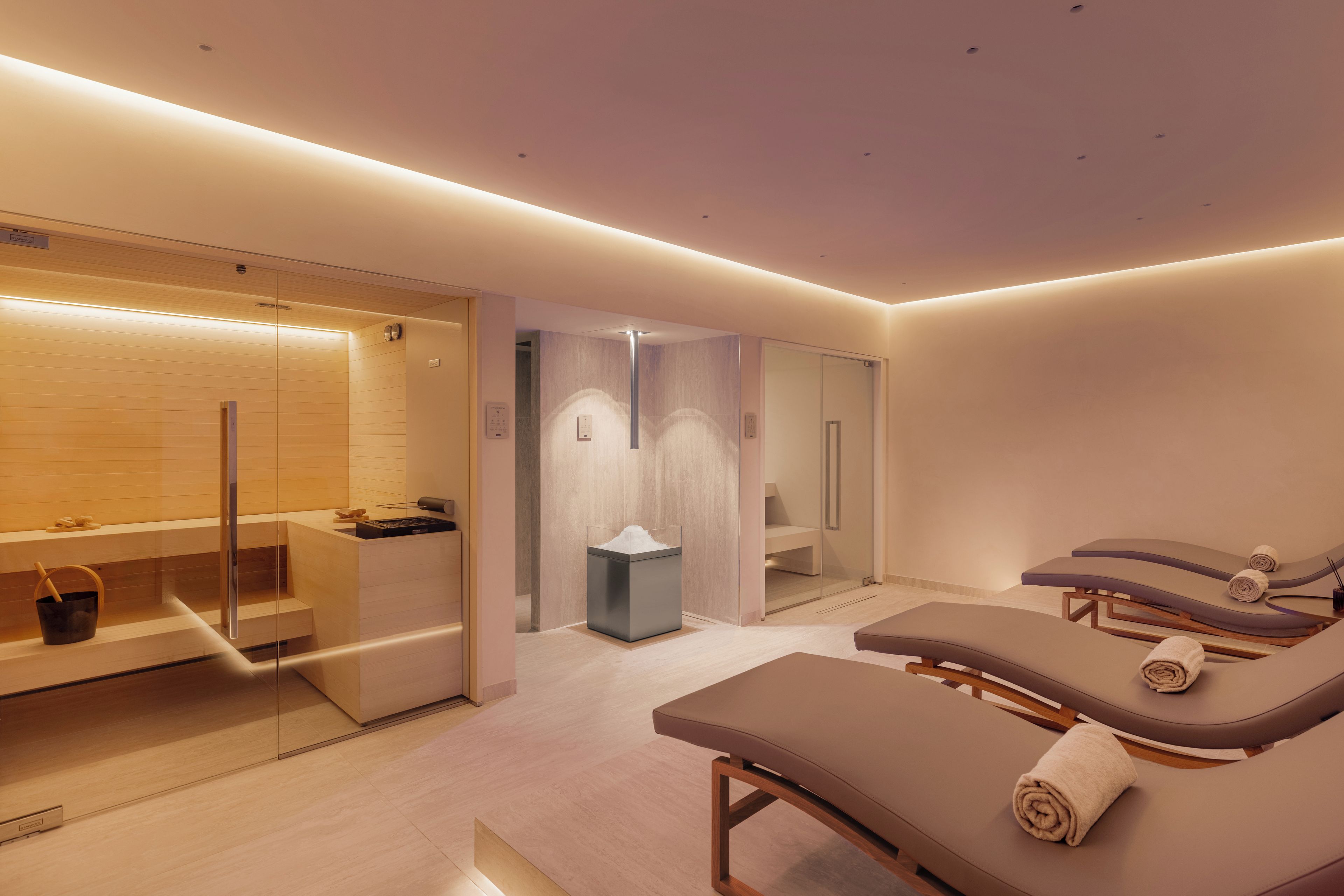 Une salle de spa moderne dotée d’une douche en verre, d’une table de massage et d’un banc en bois.