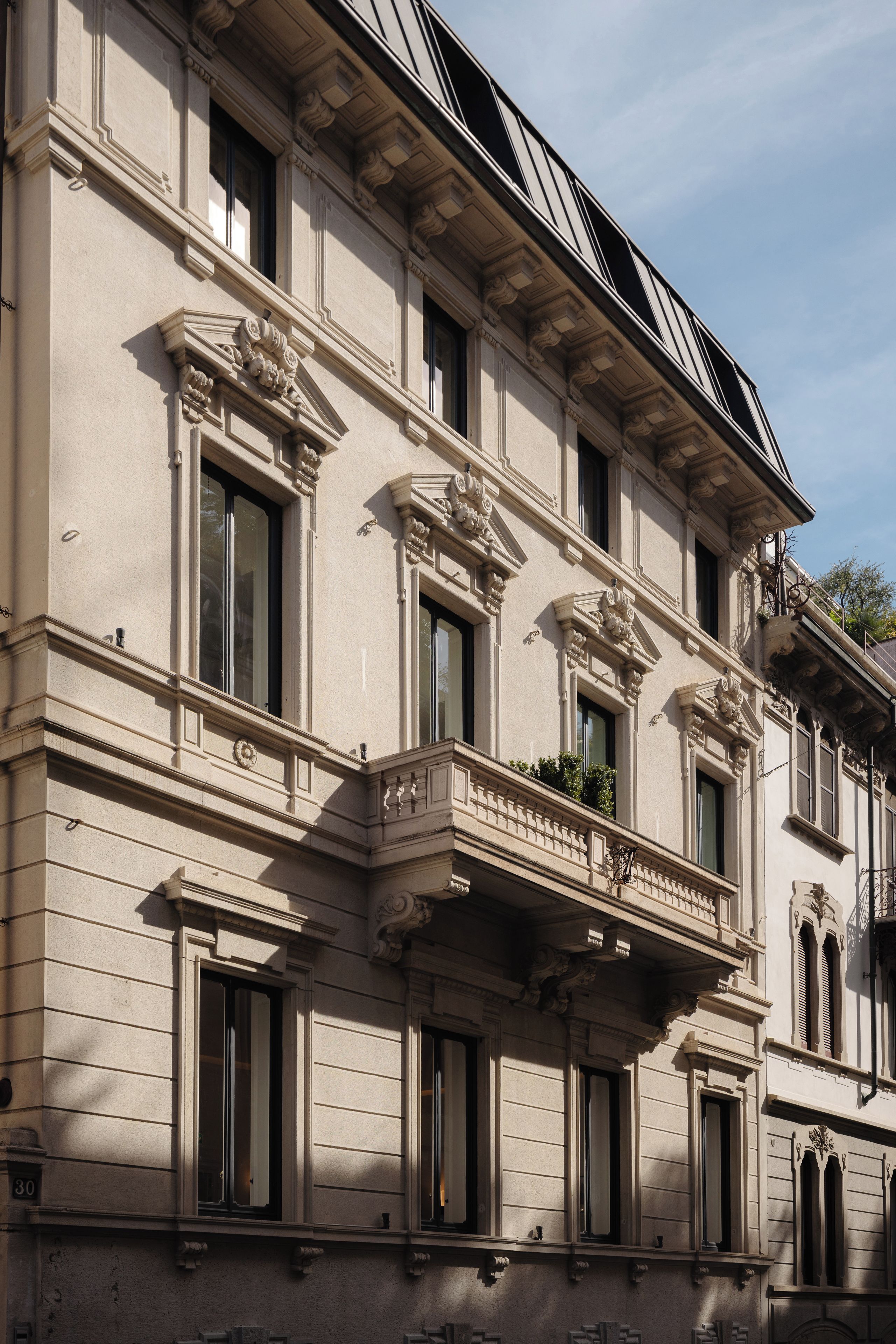 A building with classical architecture, featuring multiple windows, decorative moldings, and a balcony with plants.
