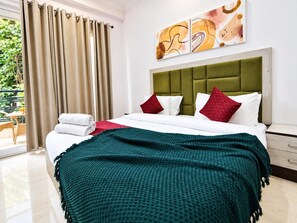Ein Hotelzimmer mit einem Bett, einem grünen Kopfteil, weißen und roten Kissen, einer türkisblauen Decke und einem Fenster mit Vorhängen.